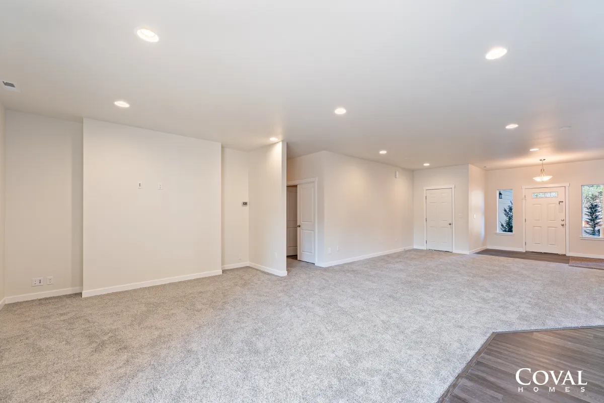 Spacious empty living room with beige carpet, white walls, recessed lights, and large windows.
