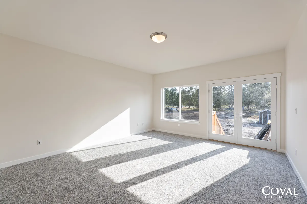 Bright empty carpeted room with white walls and large windows casting sunlight on the floor