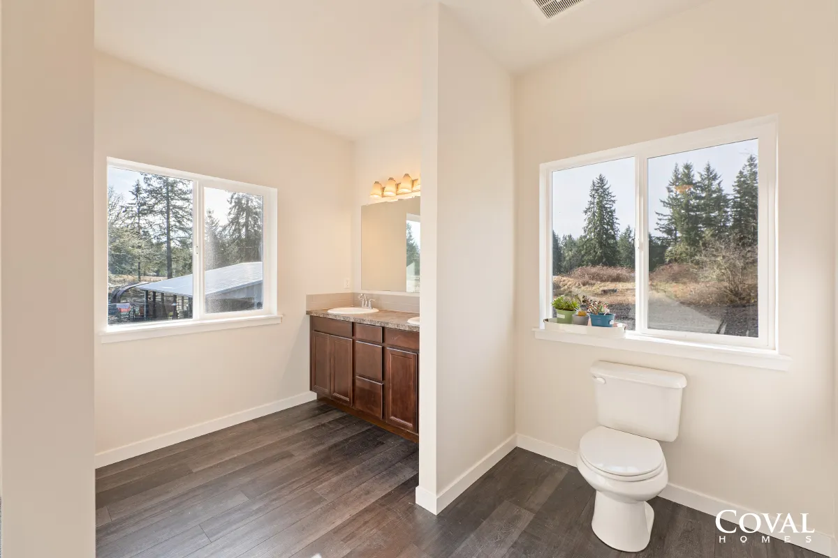 Bright bathroom with dual windows, vanity, and toilet on dark wood flooring