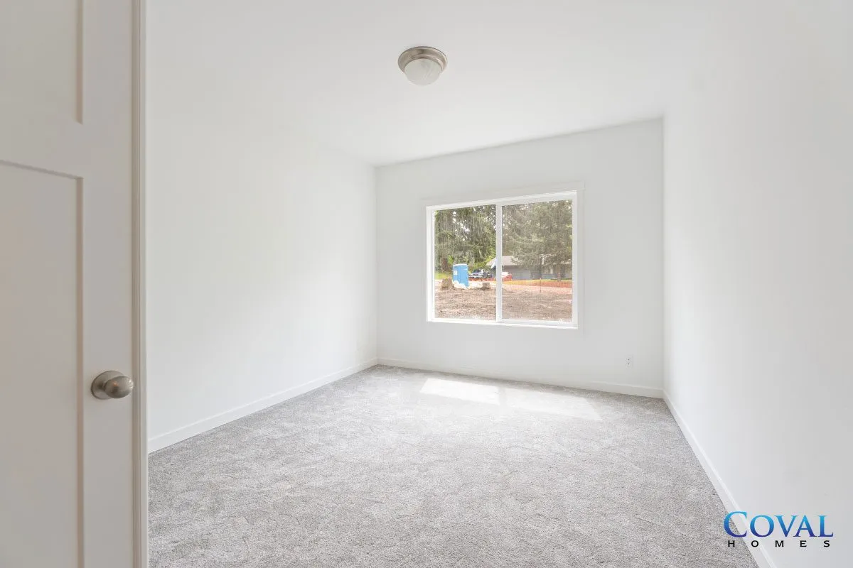 Empty white bedroom with gray carpet and a window letting in natural light