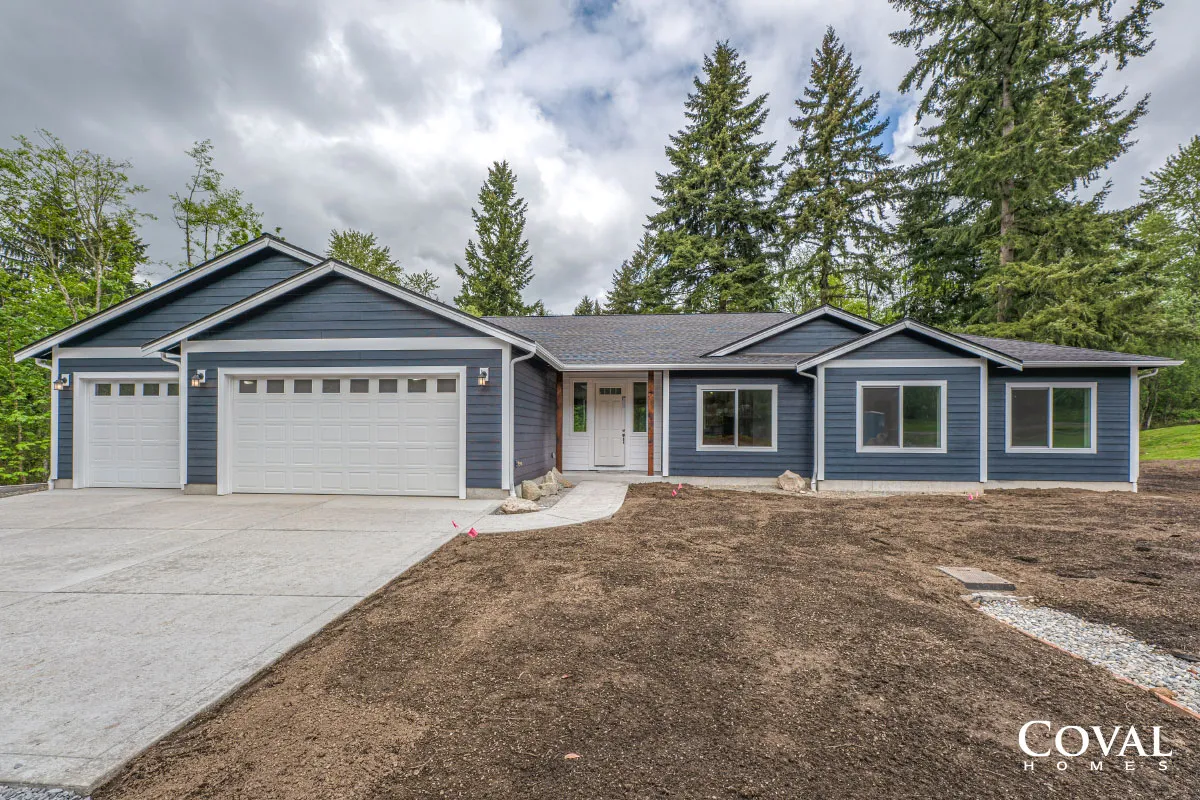 Gray single-story house with three-car garage, blue trim, and a large driveway under cloudy skies