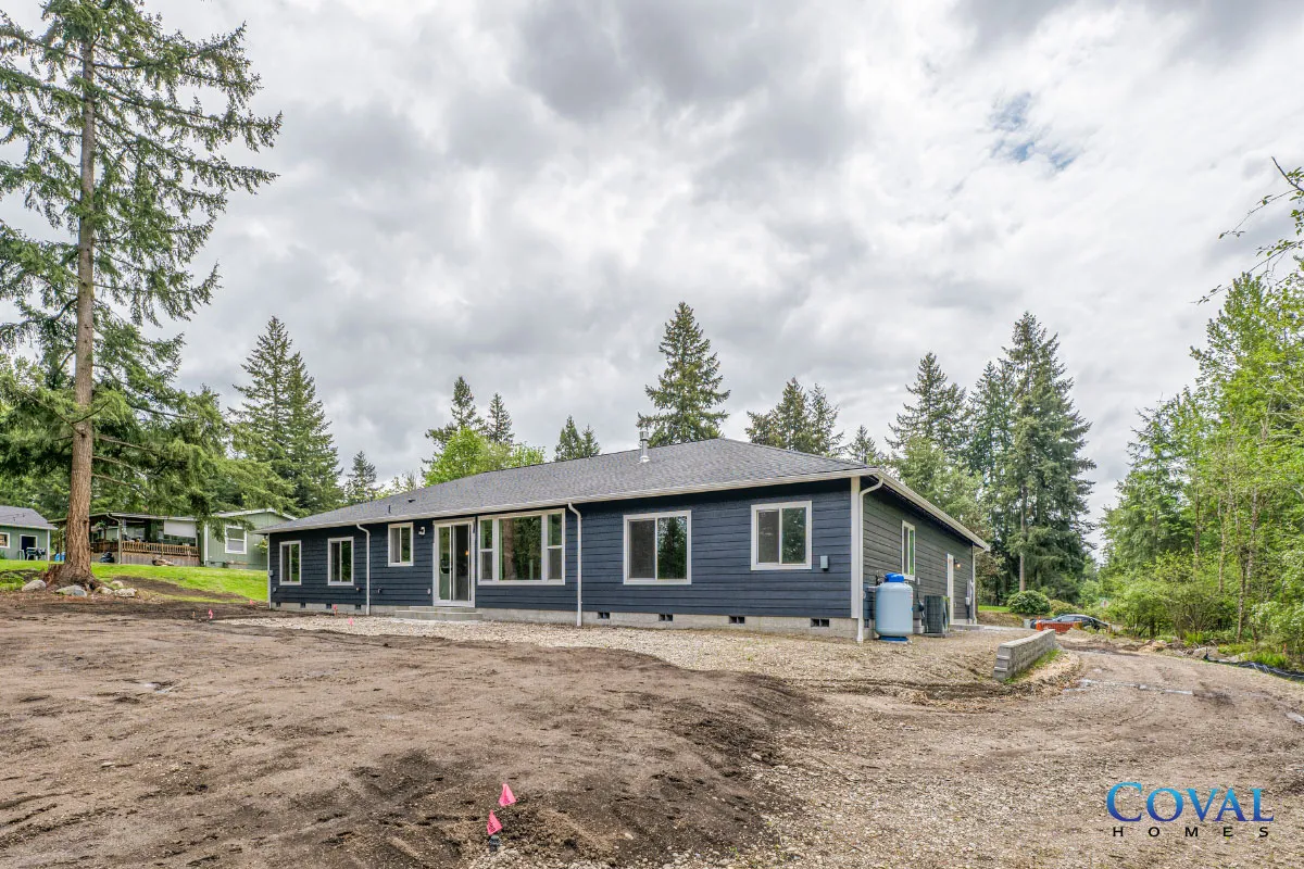 Blue single-story house in a wooded clearing under a cloudy sky