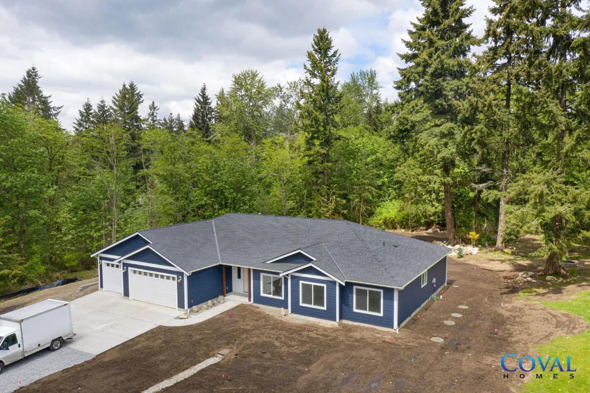 Blue single-story house with a gray roof, attached garage, and surrounding trees in a wooded area