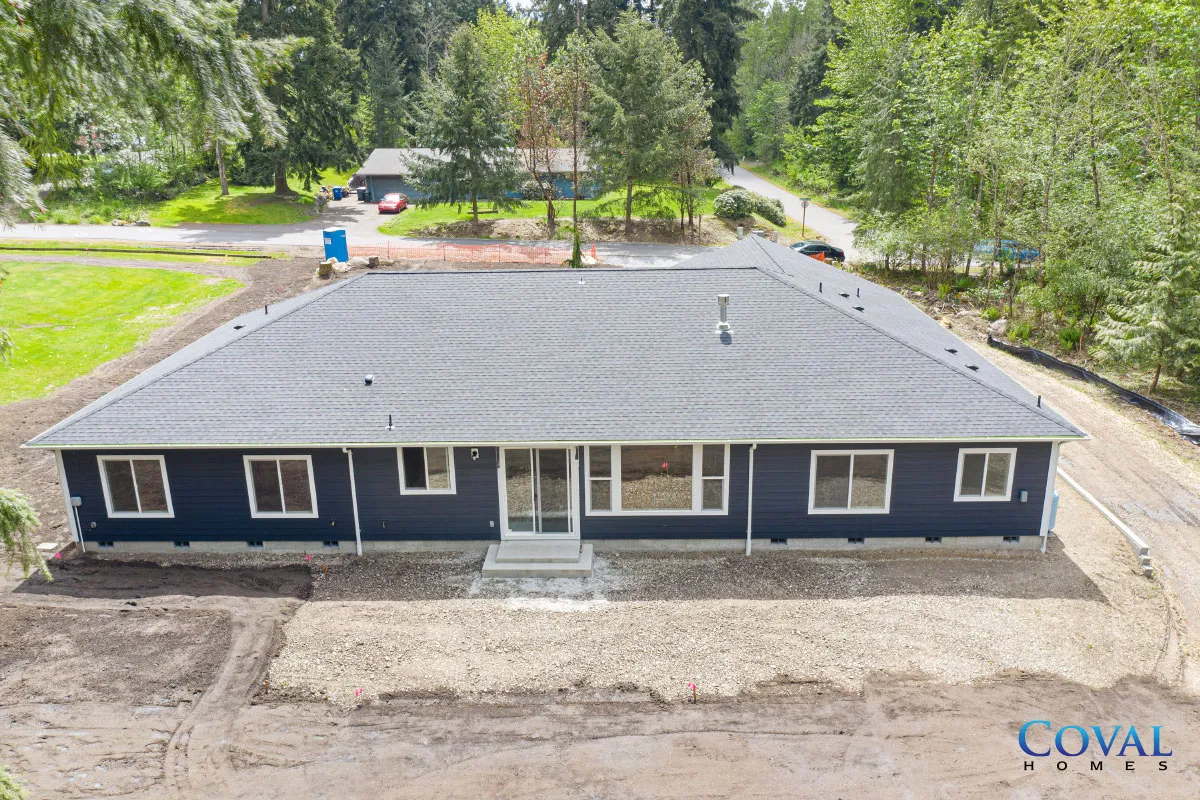 Newly built dark blue house with gray roof and front steps, viewed from above amid trees