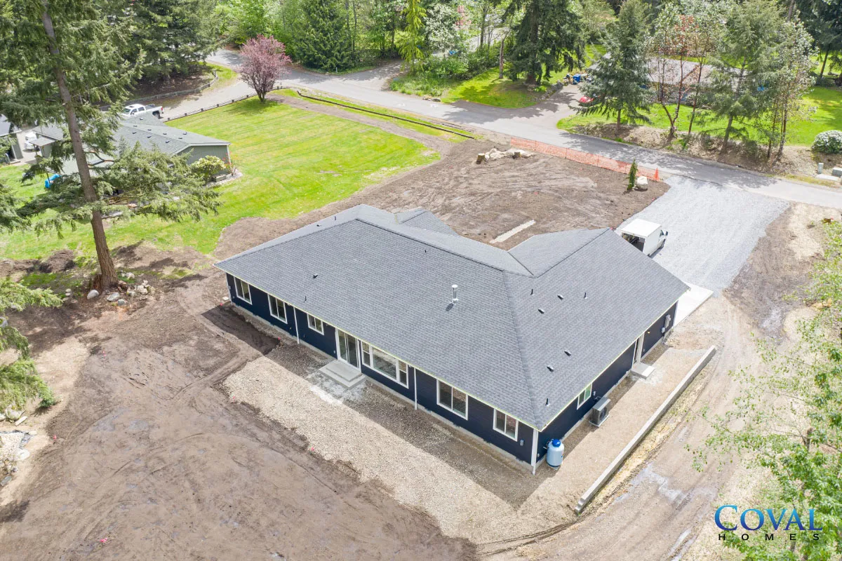 Aerial view of a new gray-roofed house on a dirt lot with surrounding trees and driveway.