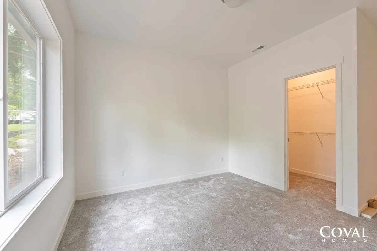 Empty white bedroom with carpet, window, and open doorway to a lit closet