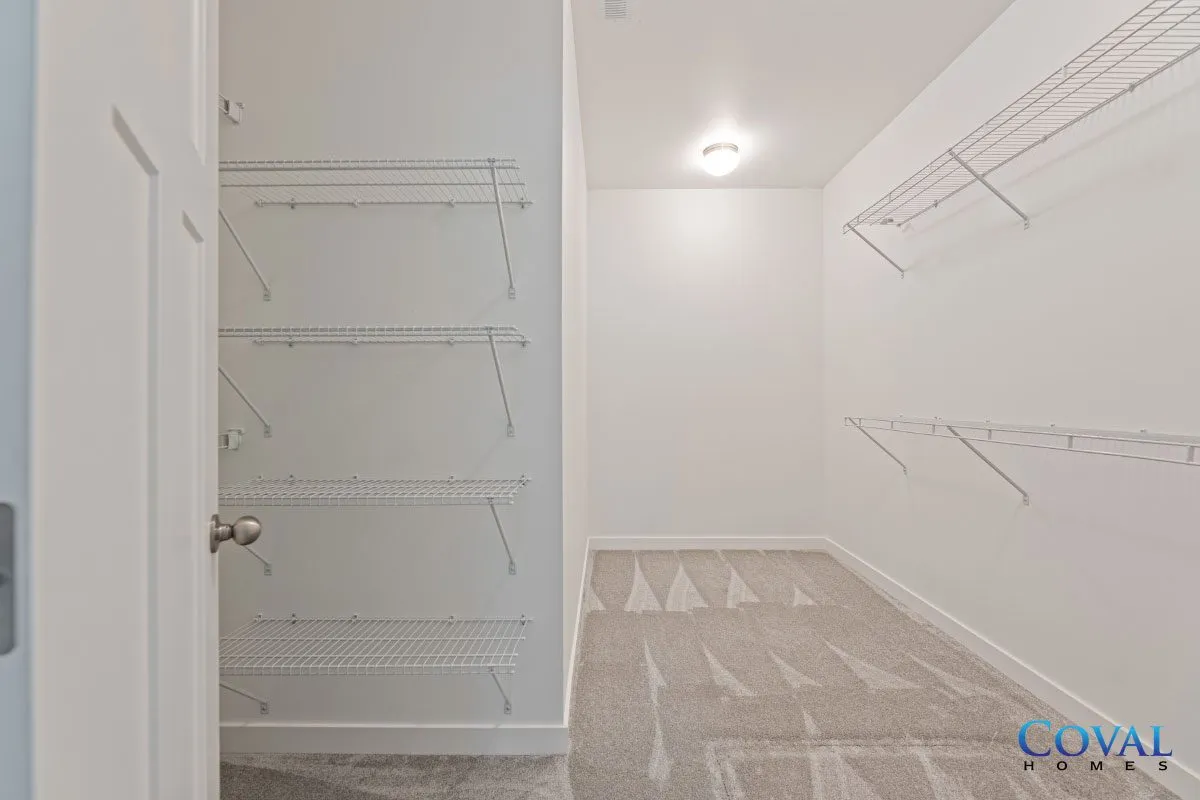 Empty walk-in closet with white wire shelves and beige carpet, viewed through an open door.