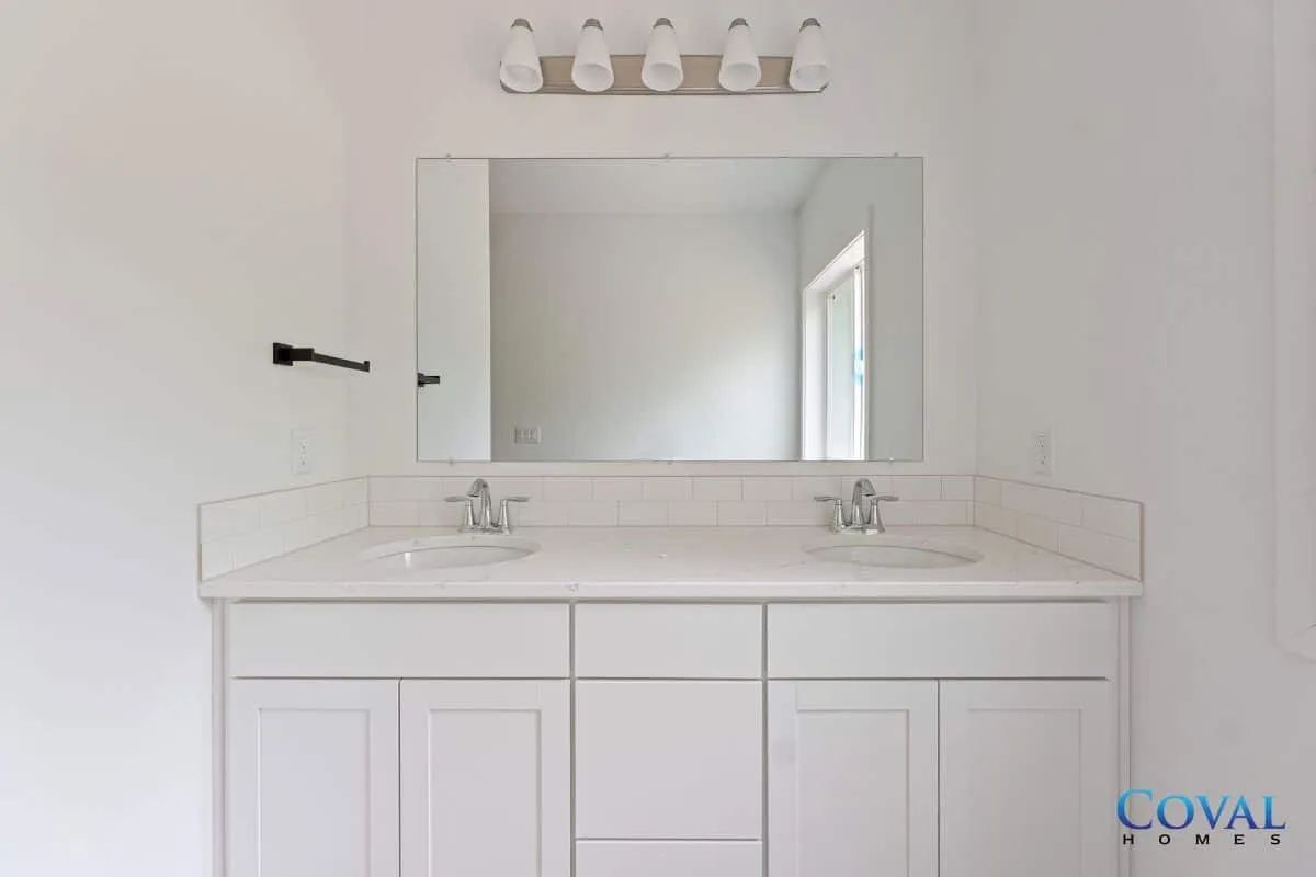 White bathroom vanity with dual sinks, large mirror, and wall light fixture