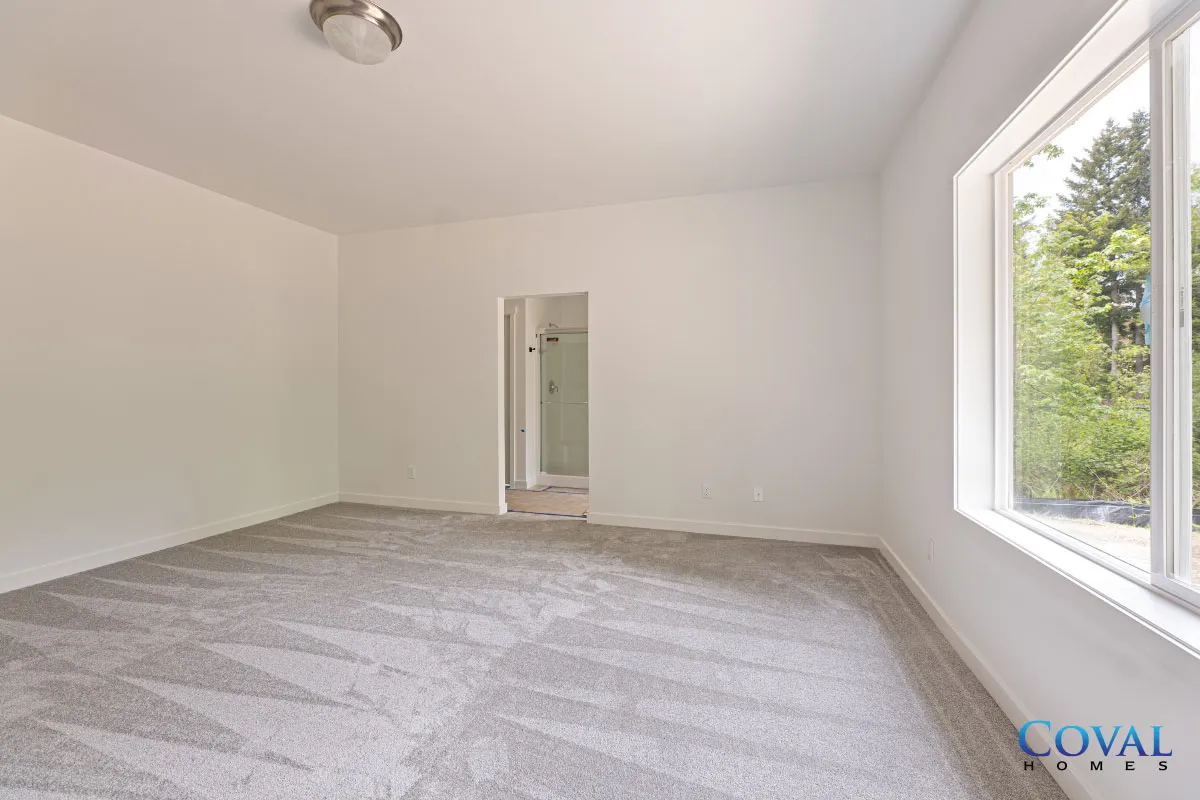 Empty white bedroom with gray carpet and large window overlooking greenery