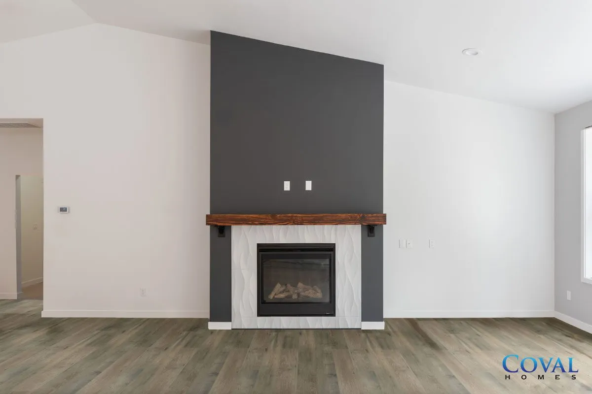 Empty modern living room with gray fireplace, dark mantel, and wood flooring