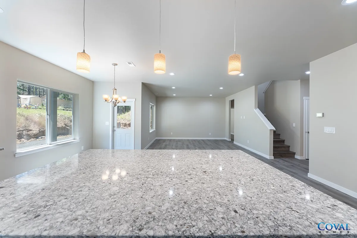 Bright open-plan living room with granite island, pendant lights, windows, and staircase to the right.