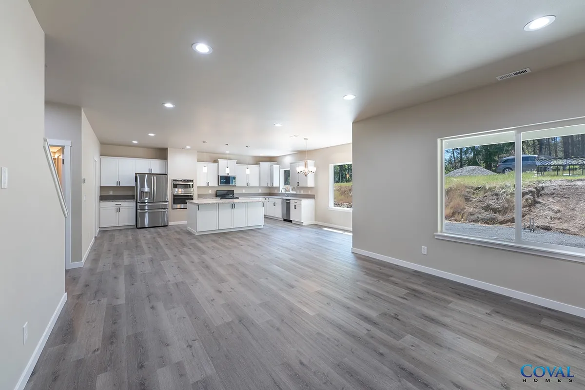 Bright open-plan kitchen and living room with gray floors, white cabinets, and large window.