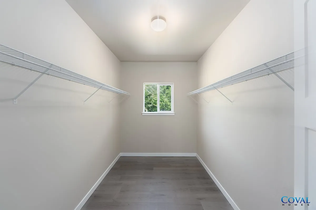 Empty white closet with wire shelves, gray floor, and a small window at the end.