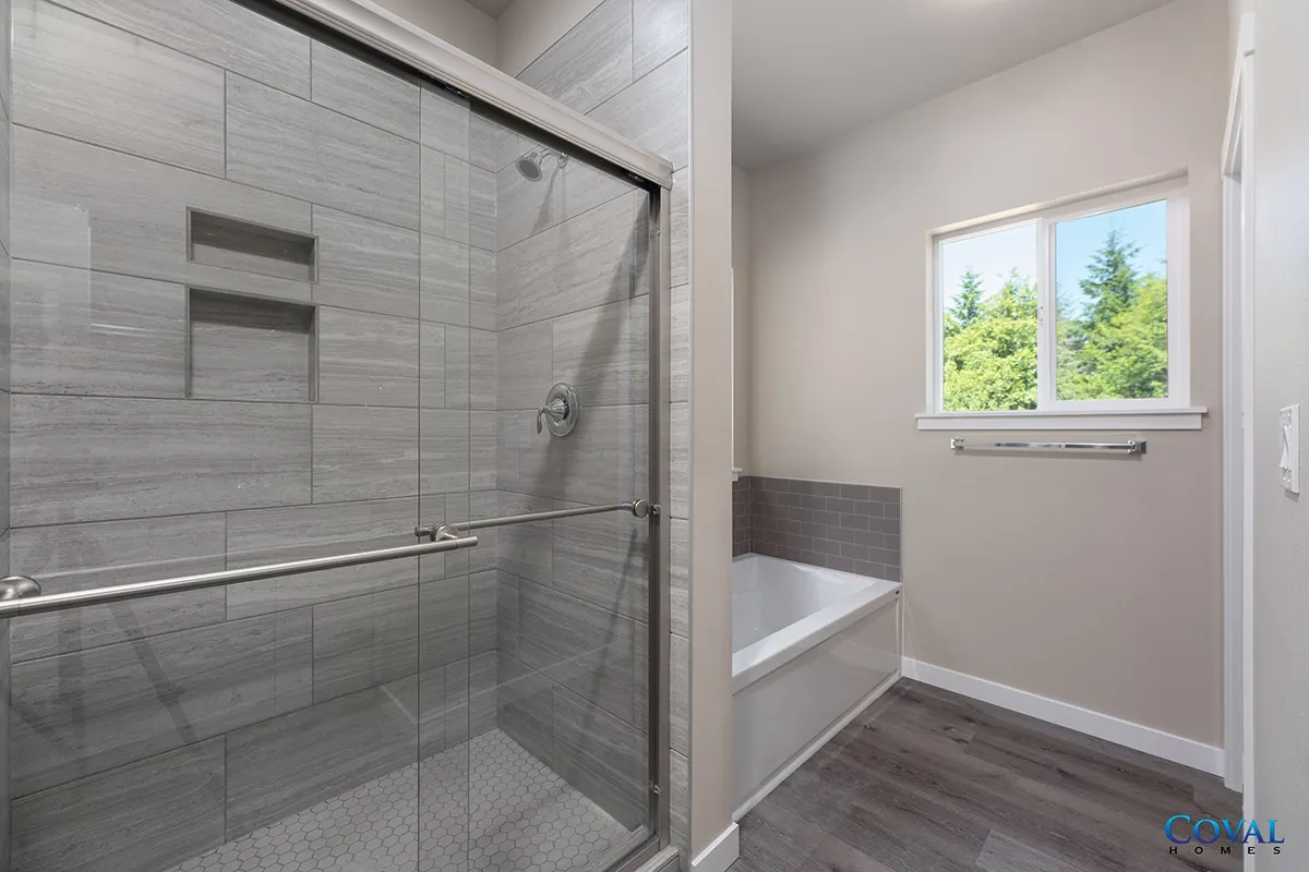 Modern bathroom with glass shower, soaking tub, gray tile, and a window with trees outside