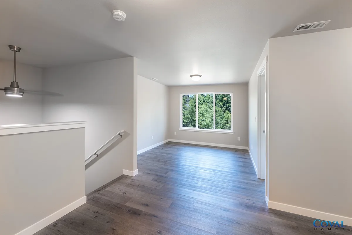 Empty modern living room with gray walls, wood floors, and large window overlooking greenery