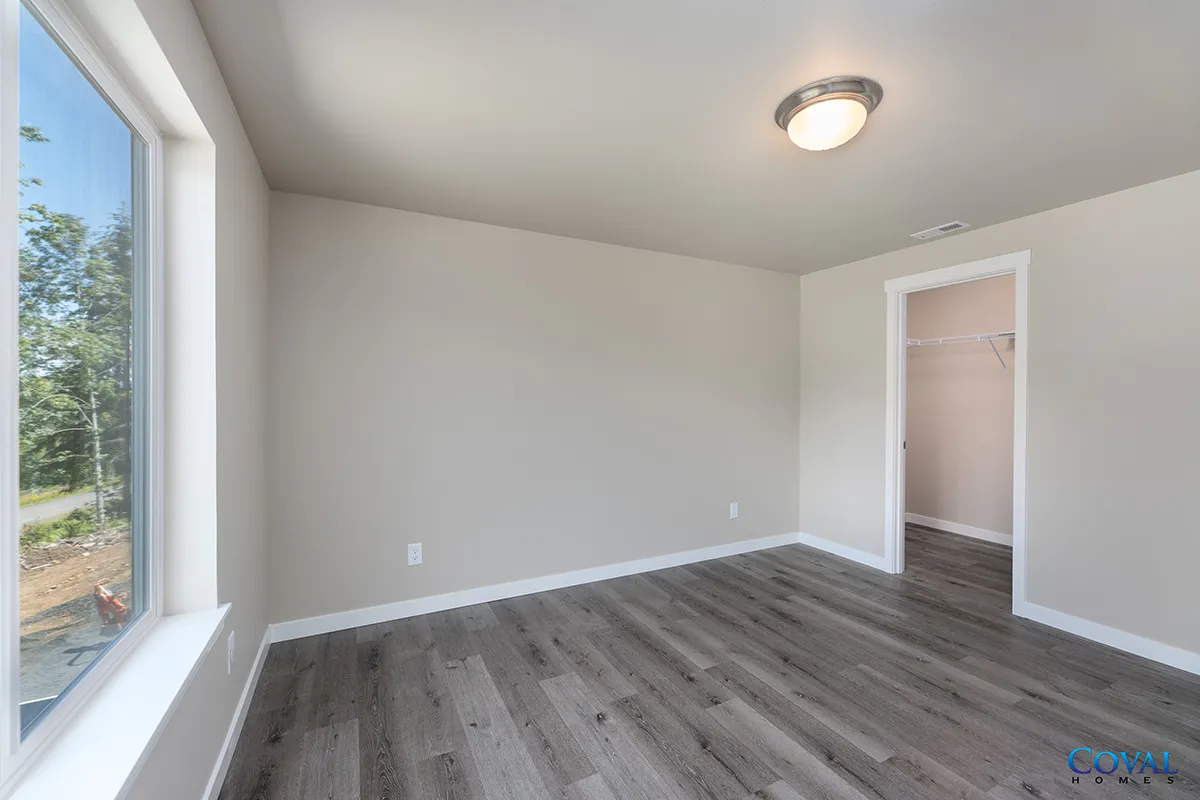 Empty bedroom with gray walls, wood-look floor, large window, and open closet door
