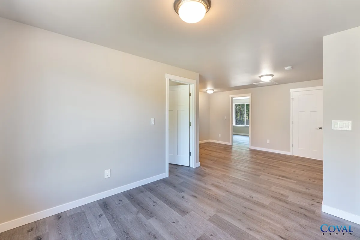 Empty room with light gray walls, wood floors, and bright windows.
