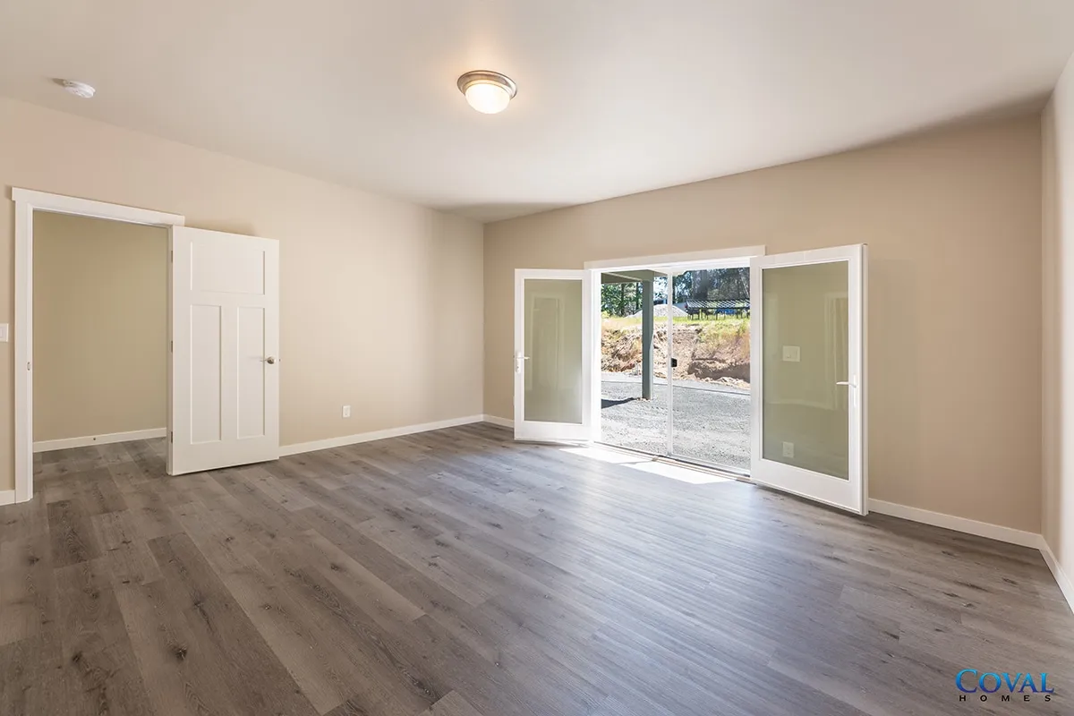Empty beige room with wood floors, open French doors, and a small adjoining closet