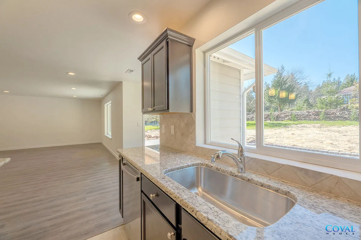 Bright kitchen with dark cabinets, granite counter, large window, and open living area.