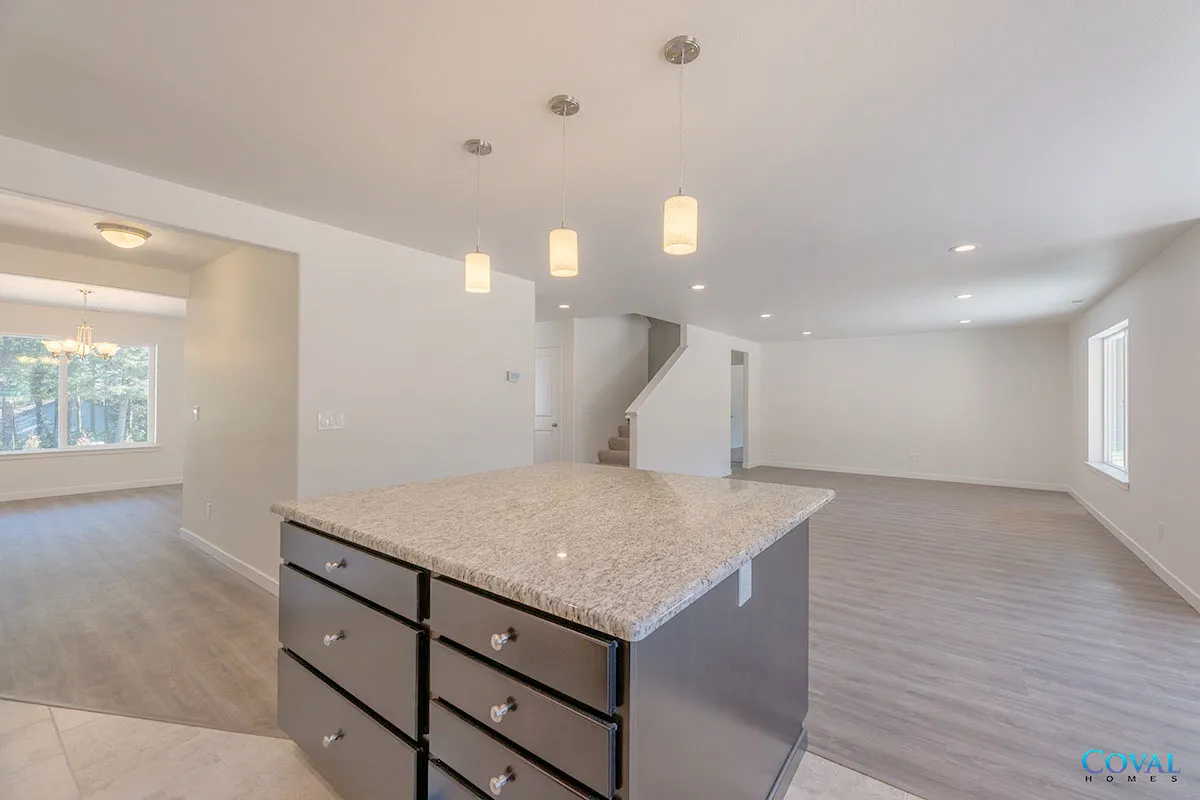 Bright, empty open-plan living space with kitchen island, light carpet, white walls, and large windows