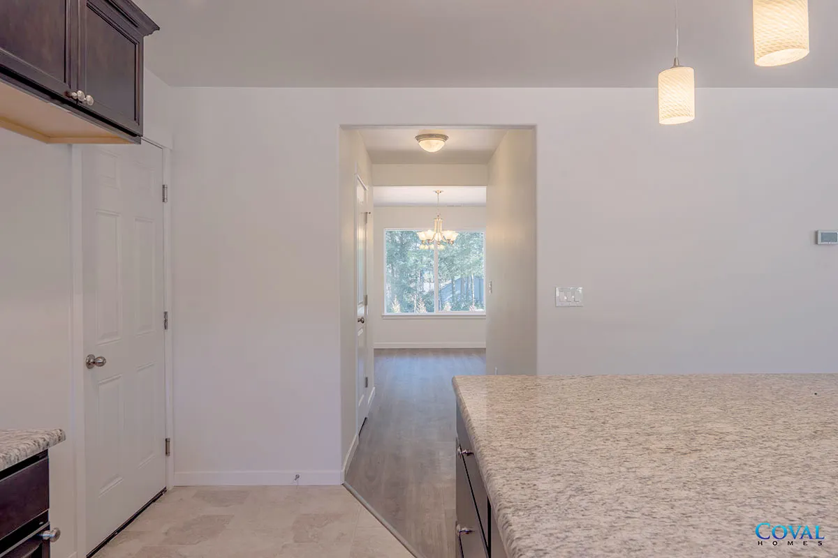 Bright kitchen with granite counter, white cabinets, and a view into a living room with a window.