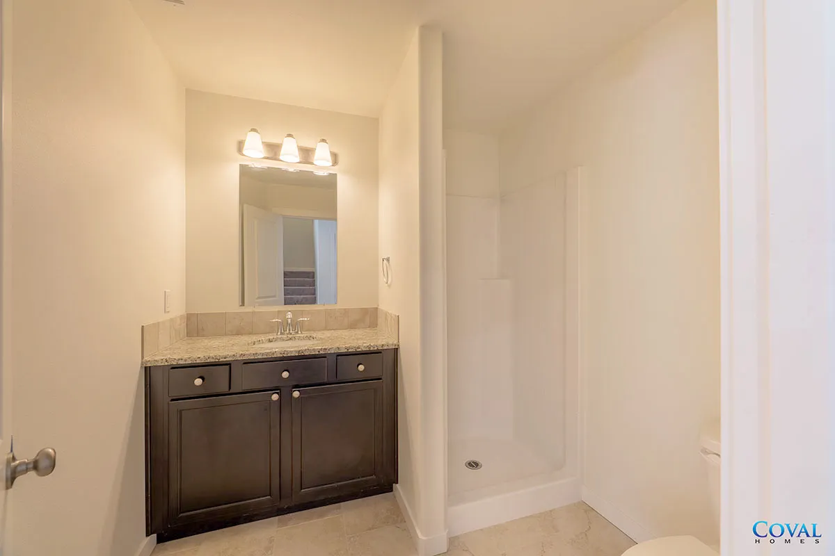 Bathroom with dark vanity, mirror light, and white shower stall in a beige room
