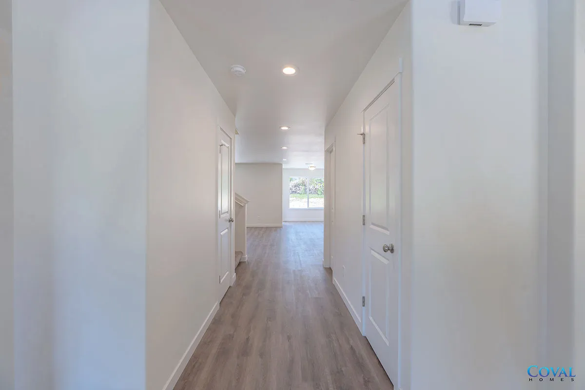 Bright modern hallway with white walls, wood flooring, and a window at the far end