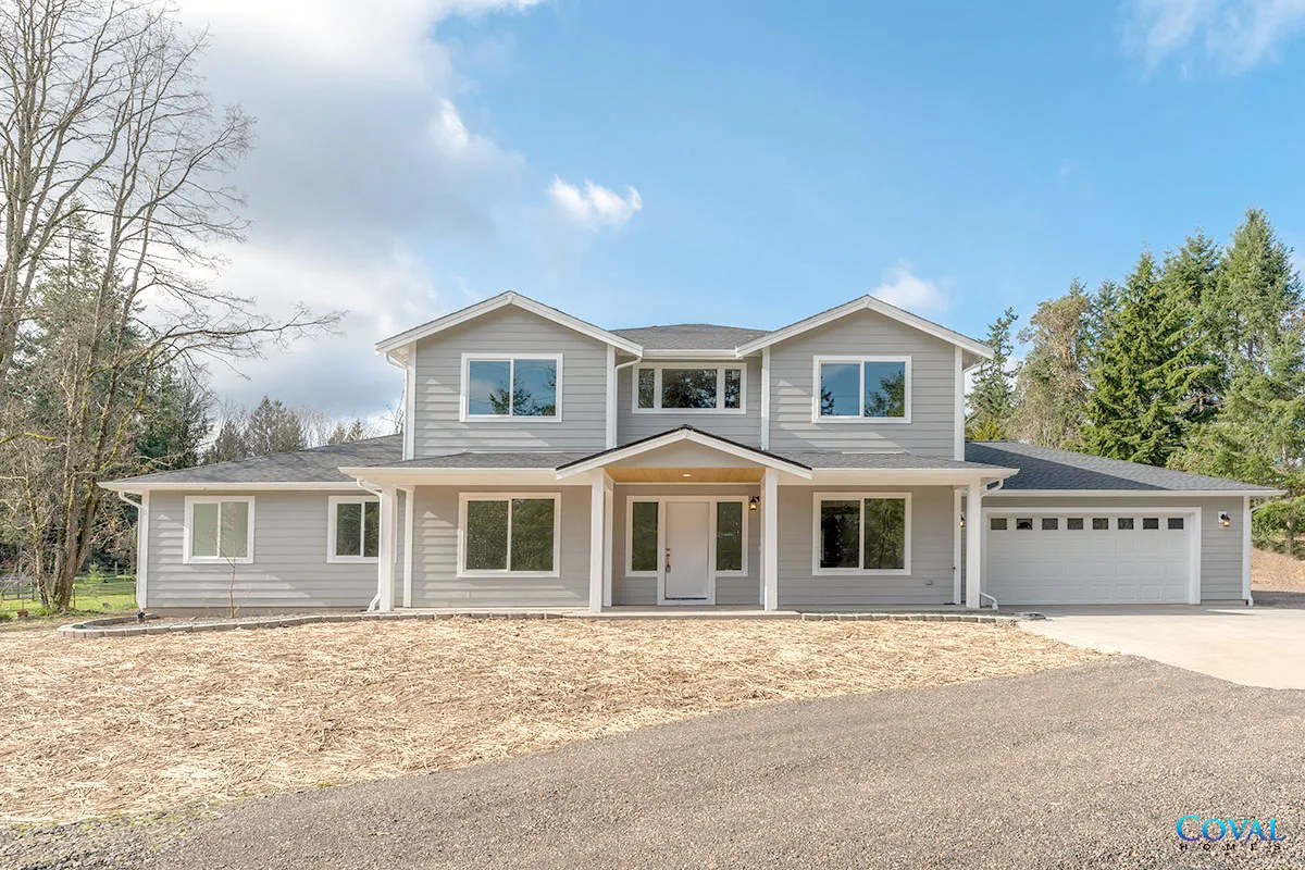 Two-story gray house with a covered porch and attached garage, set on a wooded lot