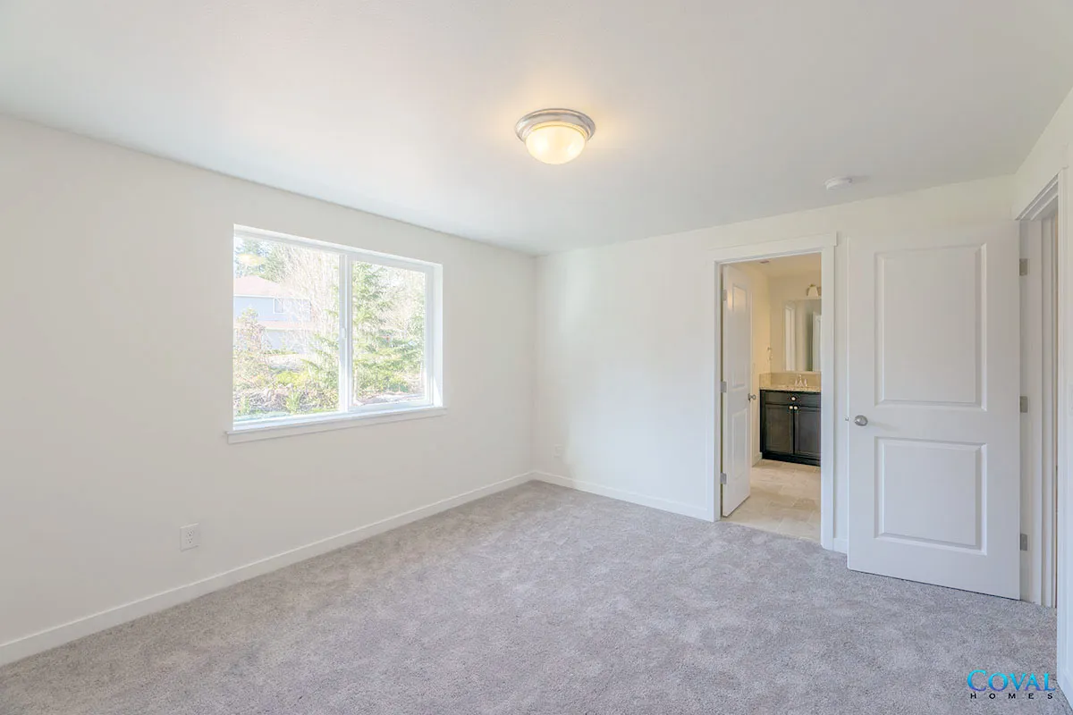 Empty white bedroom with carpet, window, ceiling light, and open door to bathroom