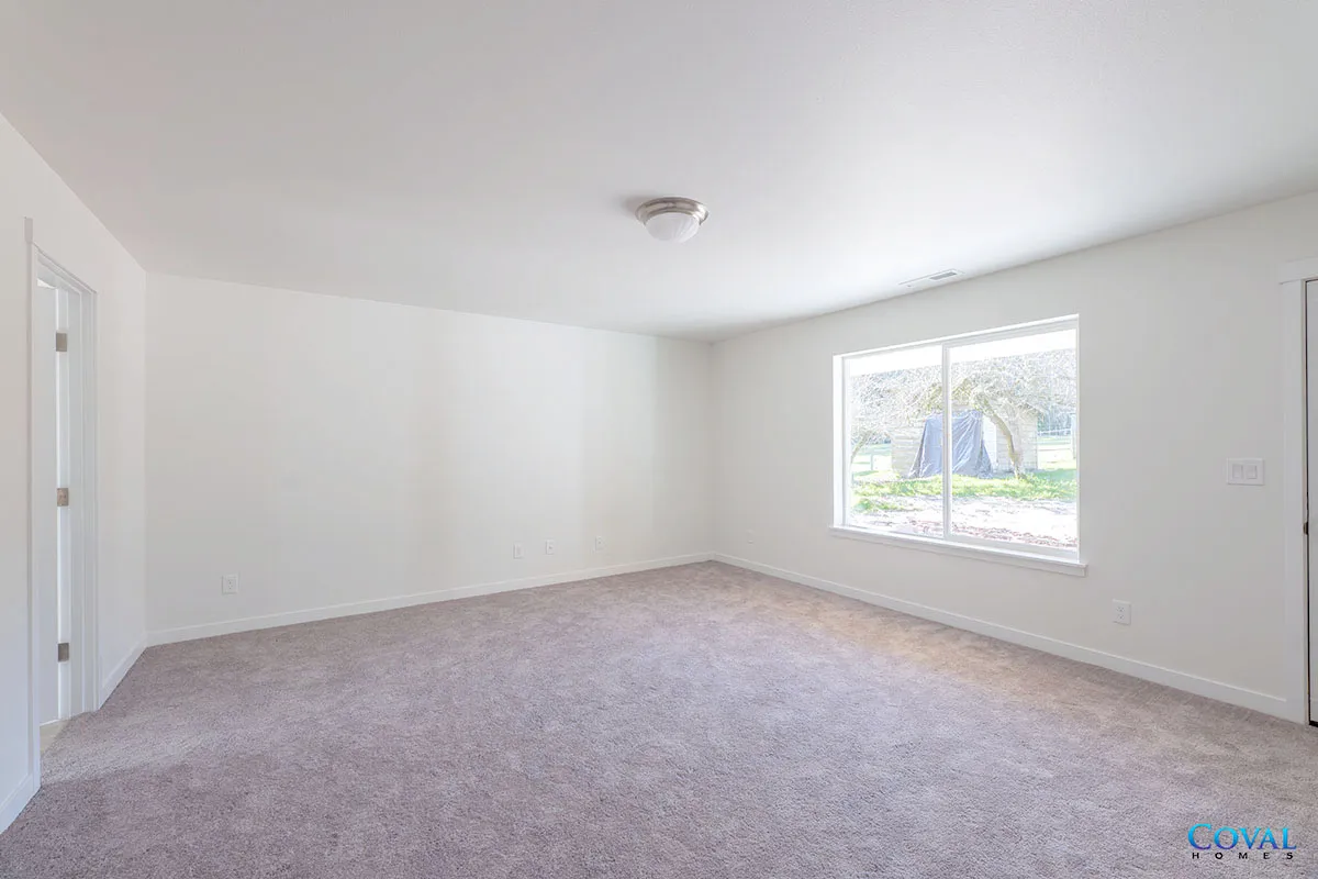 Empty white bedroom with beige carpet, window, and closet doors.