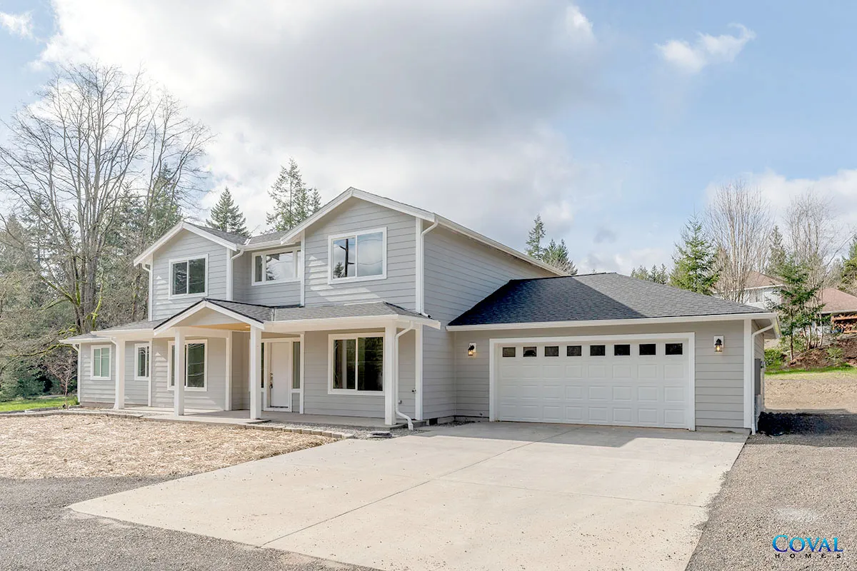 Two-story gray suburban house with attached garage and stone driveway under a partly cloudy sky