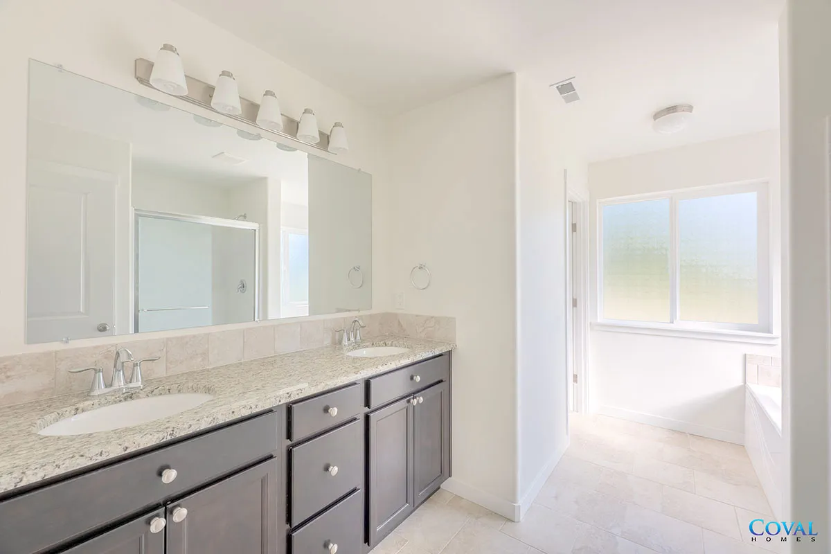 Bright bathroom vanity with double sinks, large mirror, and adjoining sunlit room with window.