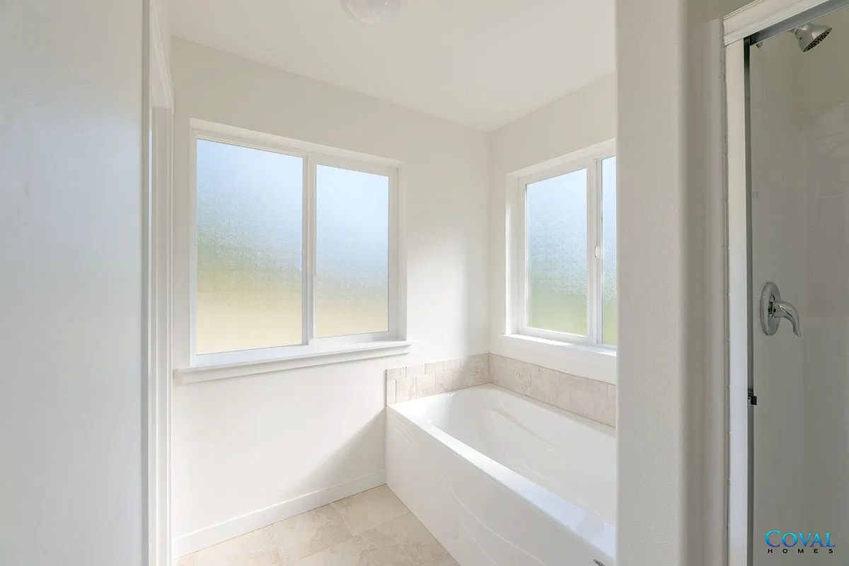 Bright white bathroom with frosted windows, a bathtub, and tiled walls.