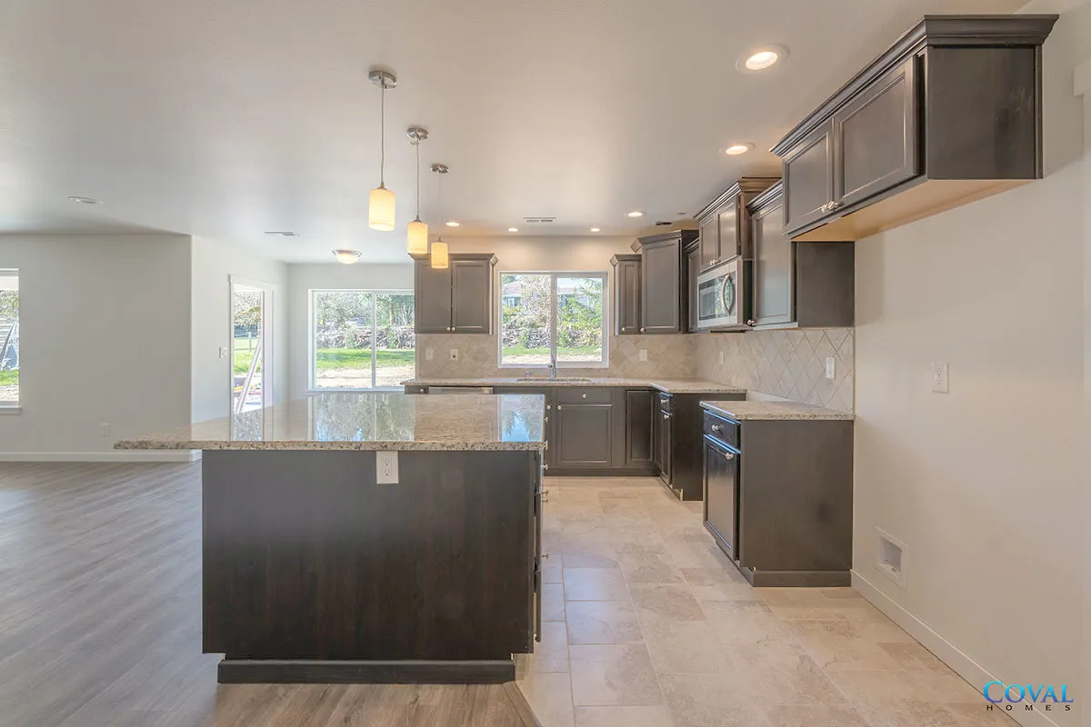 Empty modern kitchen with dark wood cabinets, island, stainless appliances, and bright windows