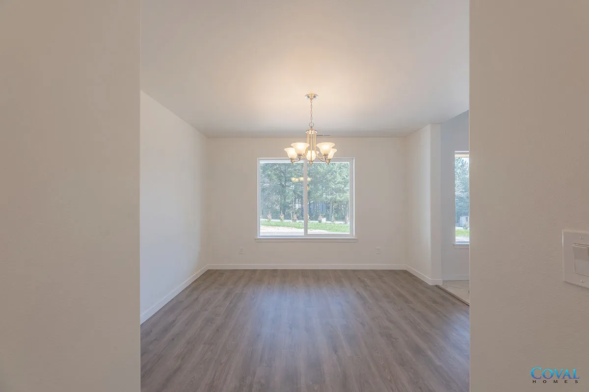Empty dining room with gray wood floors, white walls, and a chandelier by a window.