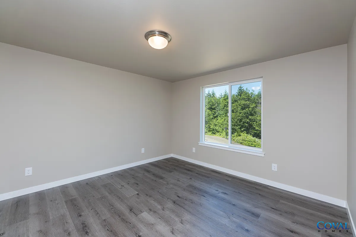 Empty gray bedroom with gray wood floors, white walls, and a window showing trees outside