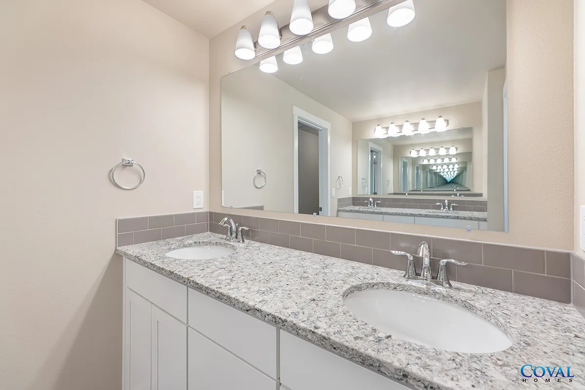 Modern bathroom vanity with granite countertop, double sinks, large mirror, and bright vanity lights