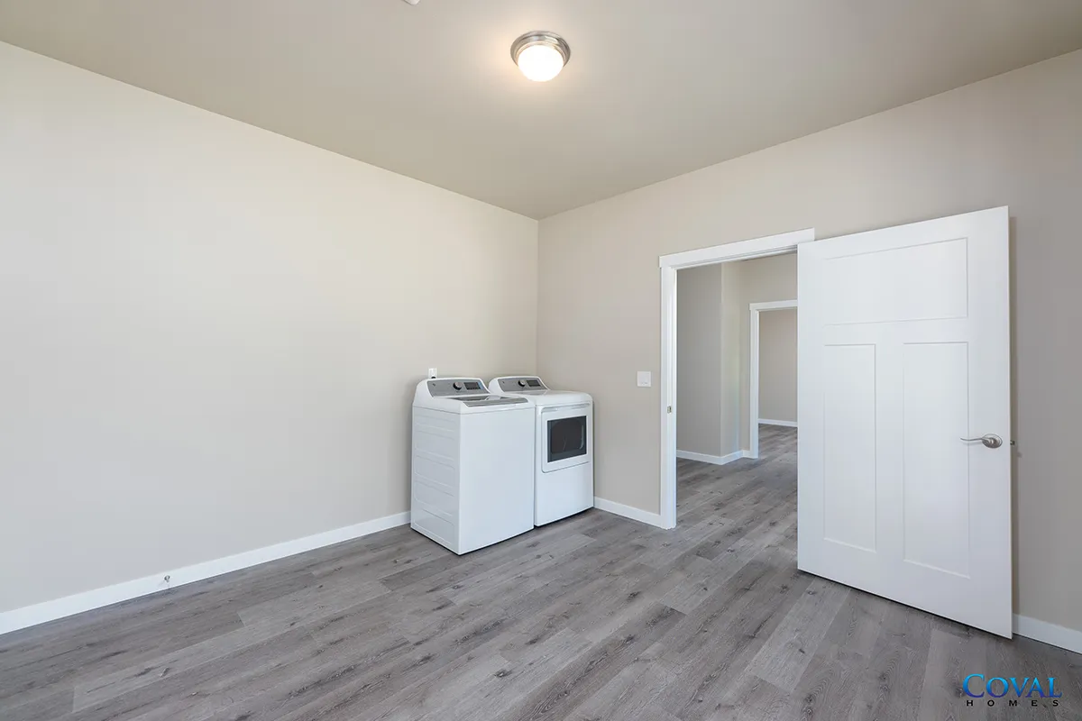 Empty laundry room with white washer and dryer, gray wood-look floors, and an open door.