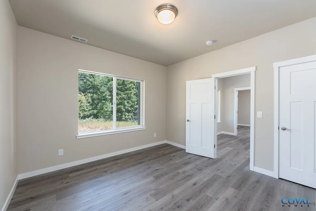 Empty beige bedroom with gray wood floors, white trim, window, and open closet doors