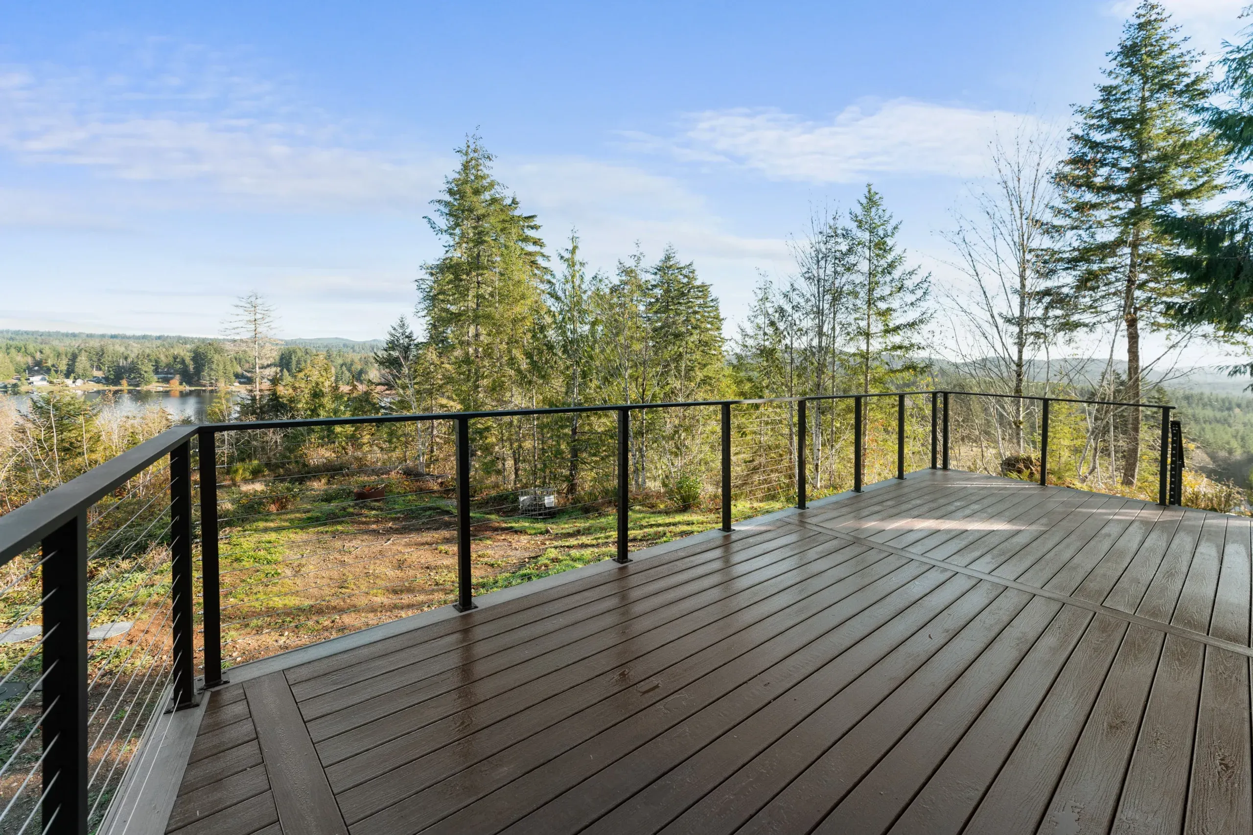Wooden deck with black railing overlooking a forested landscape under a blue sky