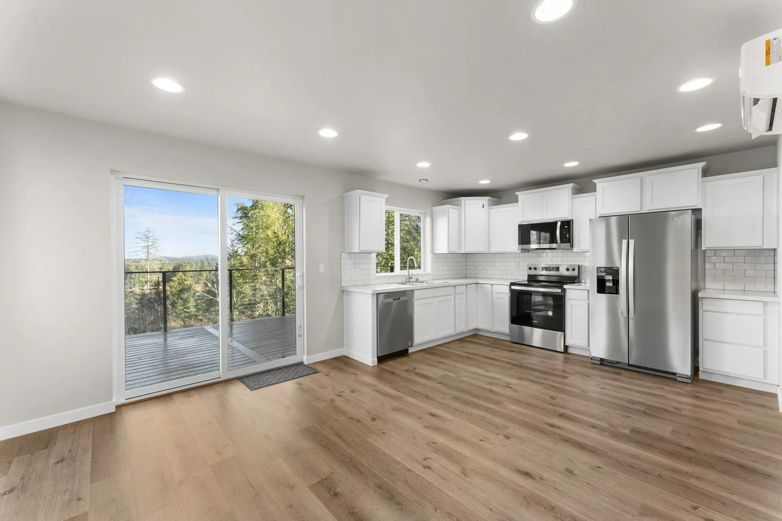 Bright modern kitchen with white cabinets, stainless appliances, wood floors, and sliding glass doors.