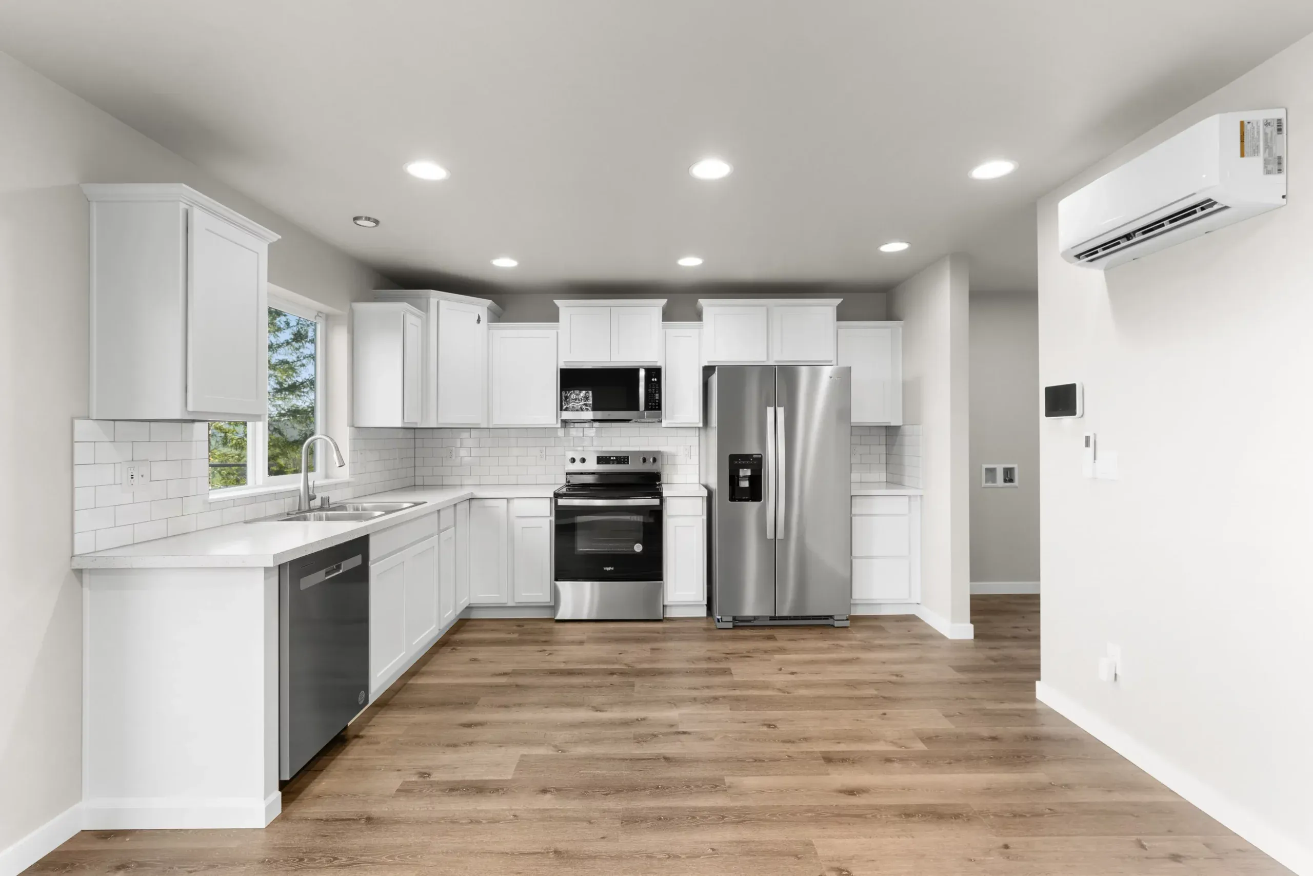 Bright modern kitchen with white cabinets, stainless appliances, and wood floors