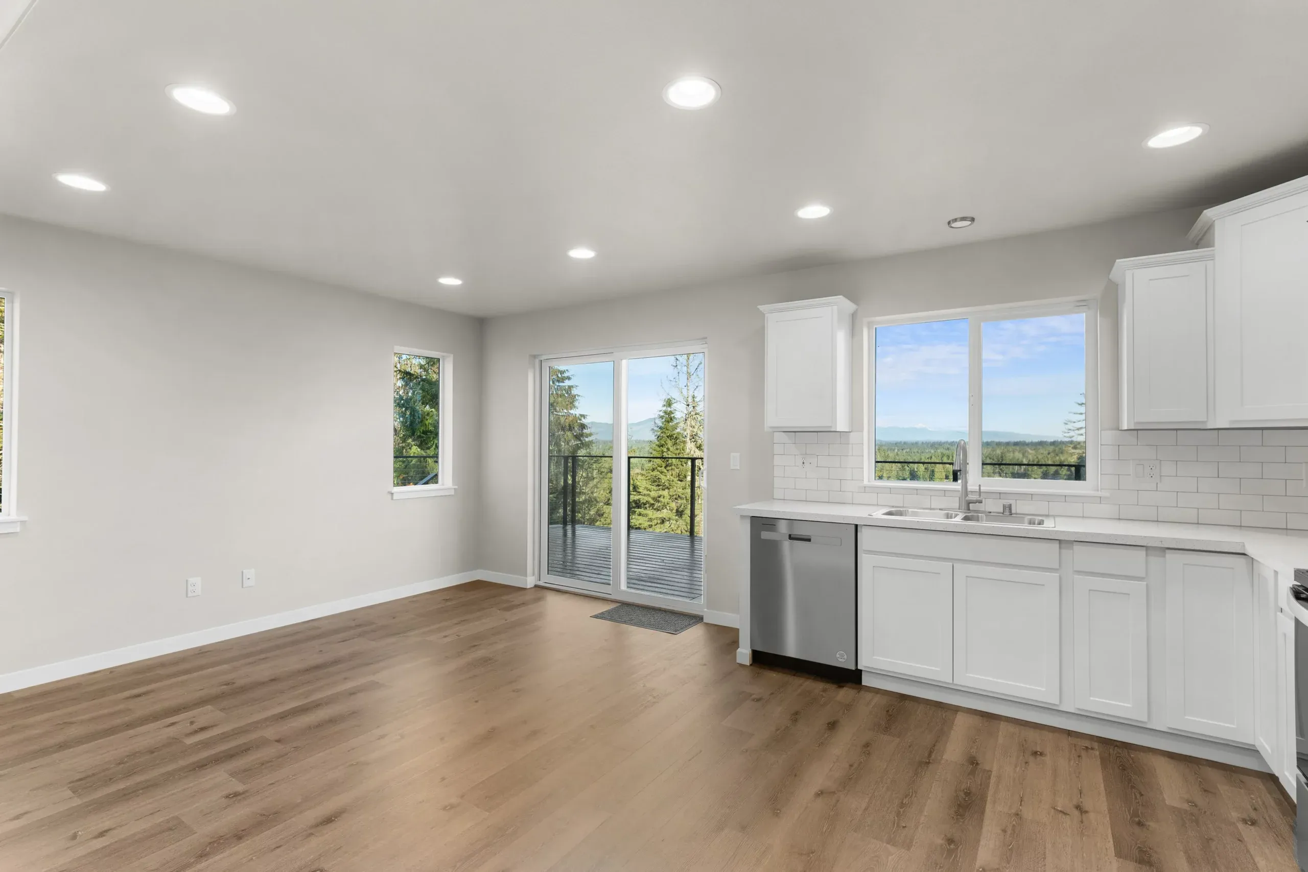 Bright empty kitchen and dining area with white cabinets, wood floors, and sliding glass doors to a balcony.