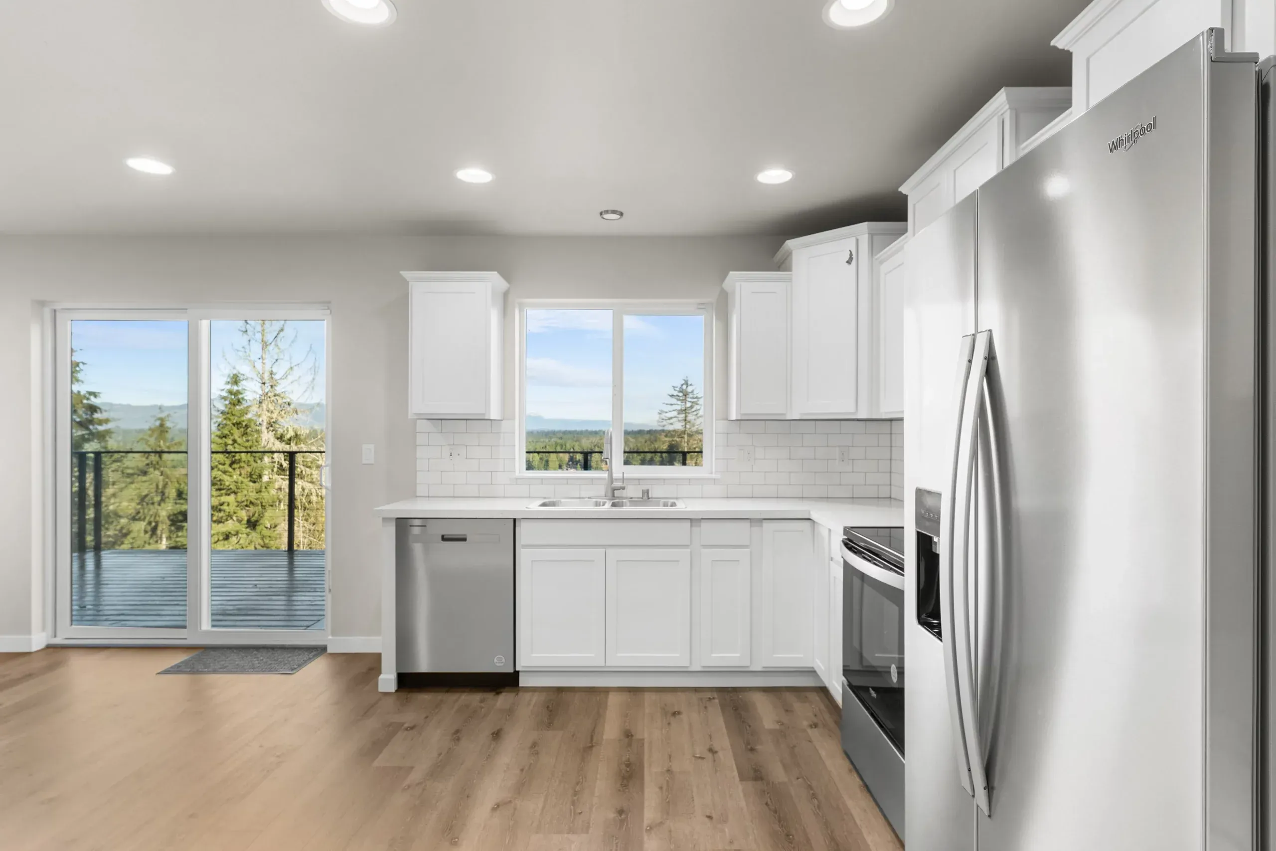 Bright modern kitchen with white cabinets, stainless appliances, wood floors, and sliding glass doors to a balcony