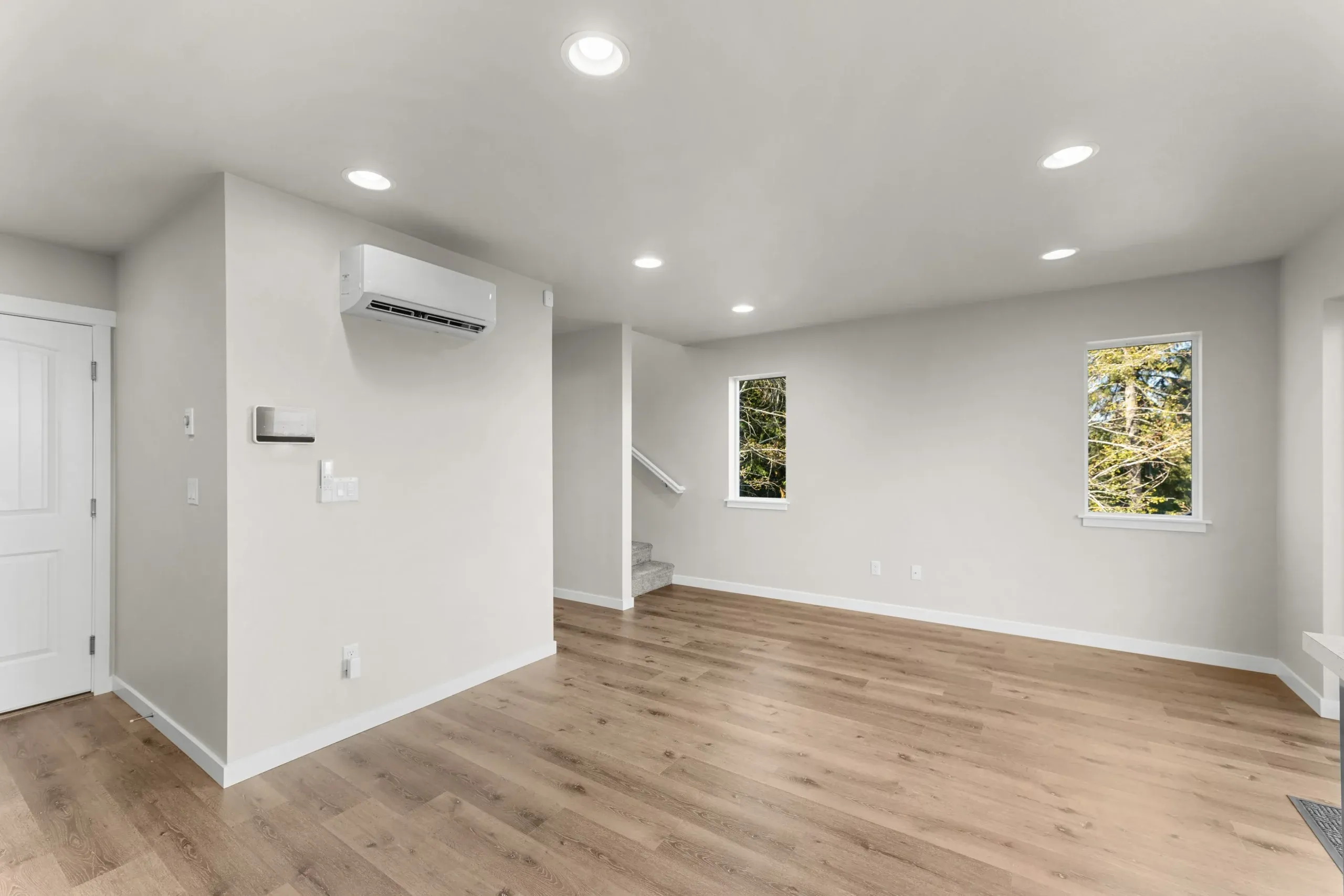 Empty modern living room with white walls, wood floors, recessed lights, and two windows