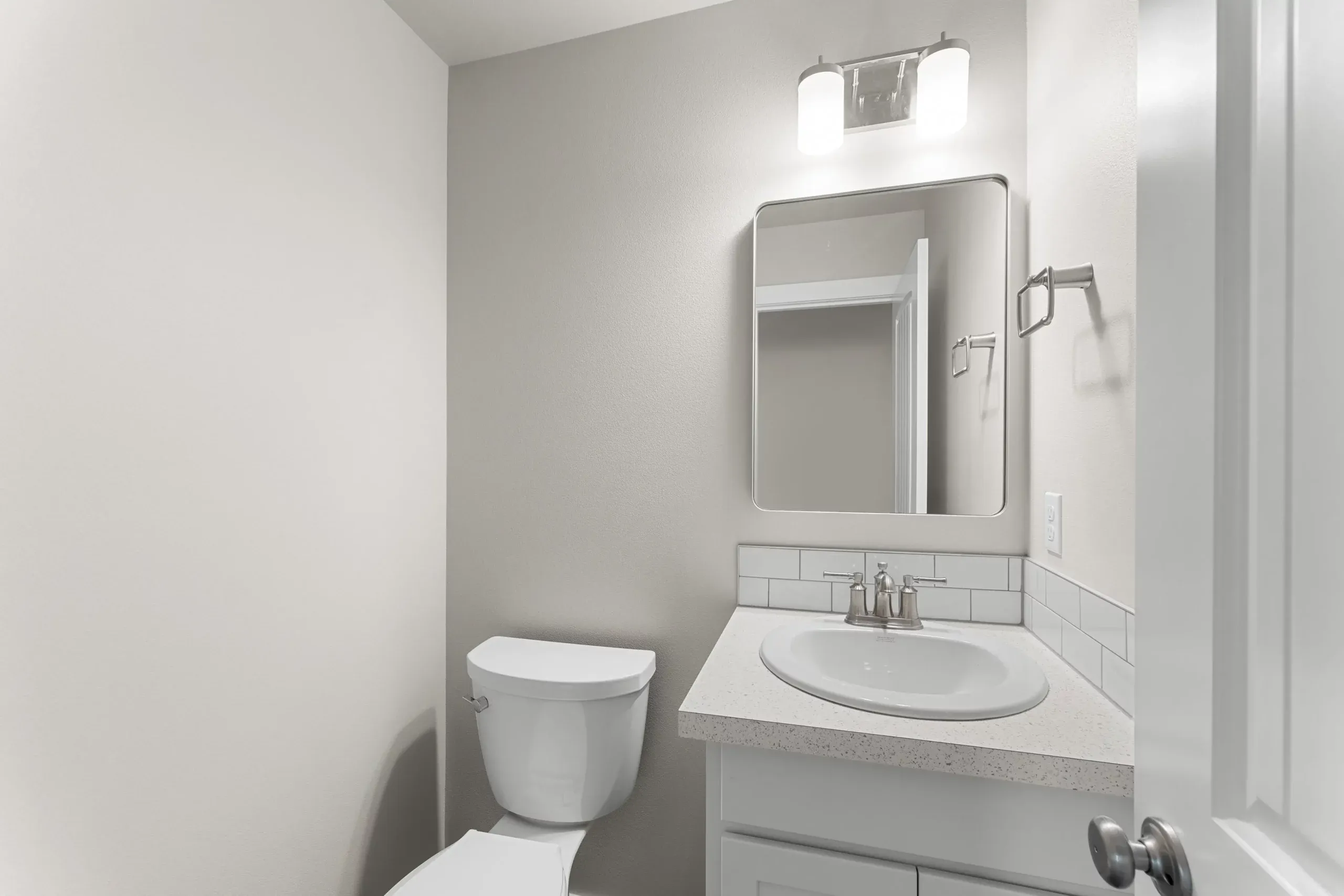 Small white bathroom with toilet, vanity sink, mirror, and wall light.