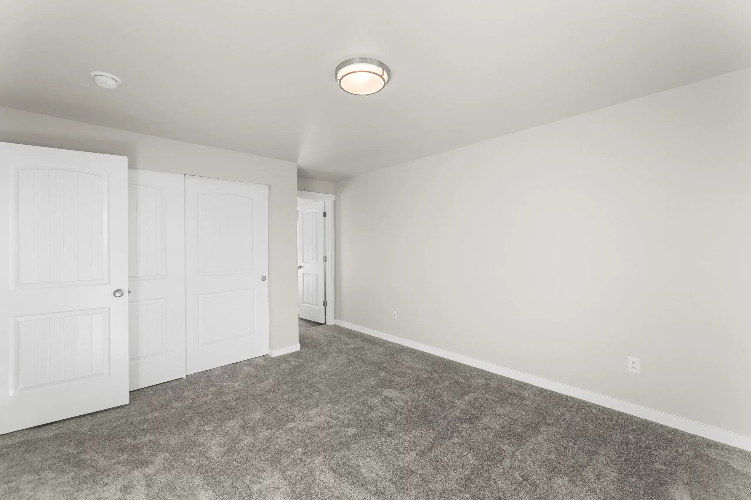 Empty white bedroom with gray carpet and two closet doors