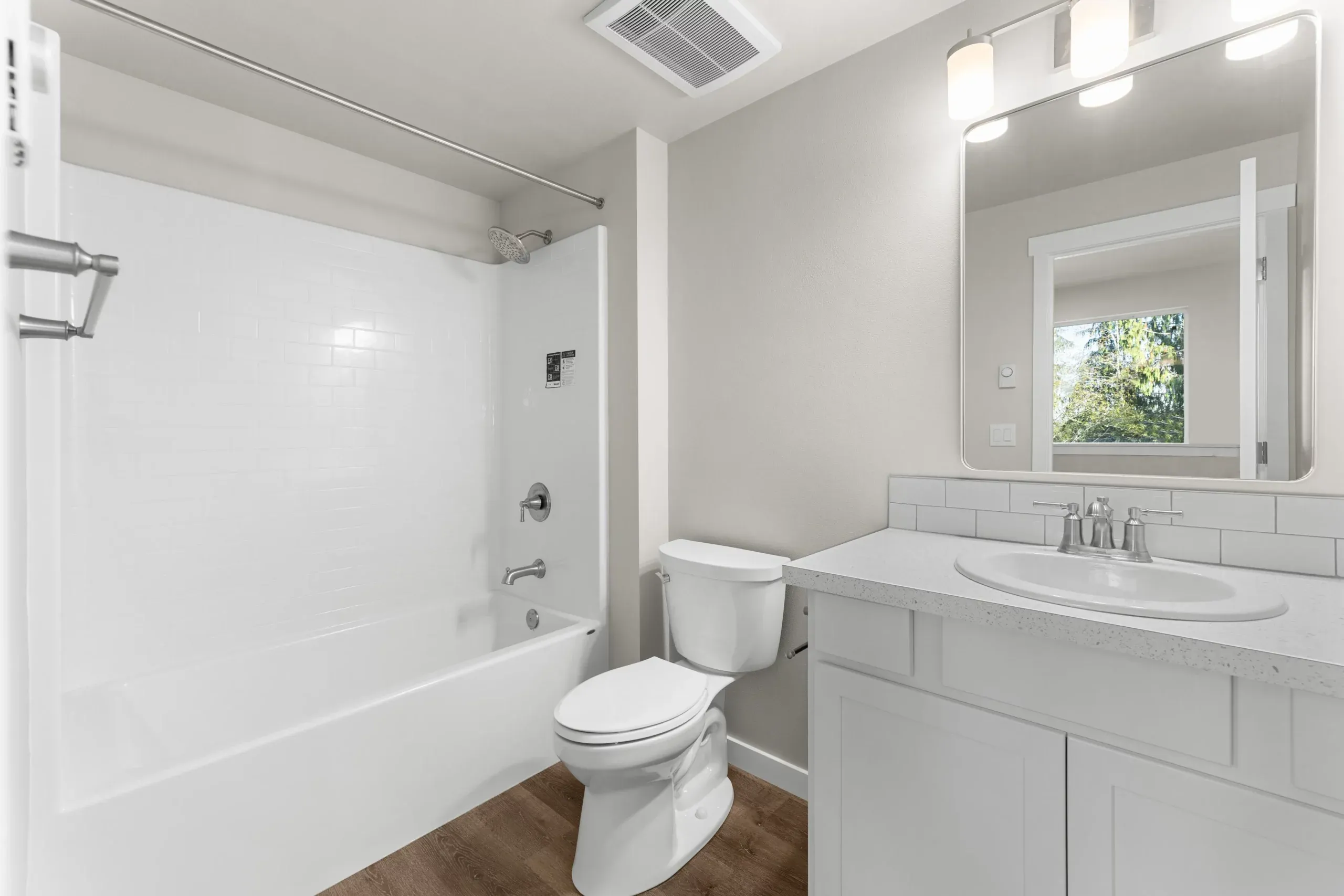 Bright white bathroom with tub, toilet, vanity, and mirror under wall lights