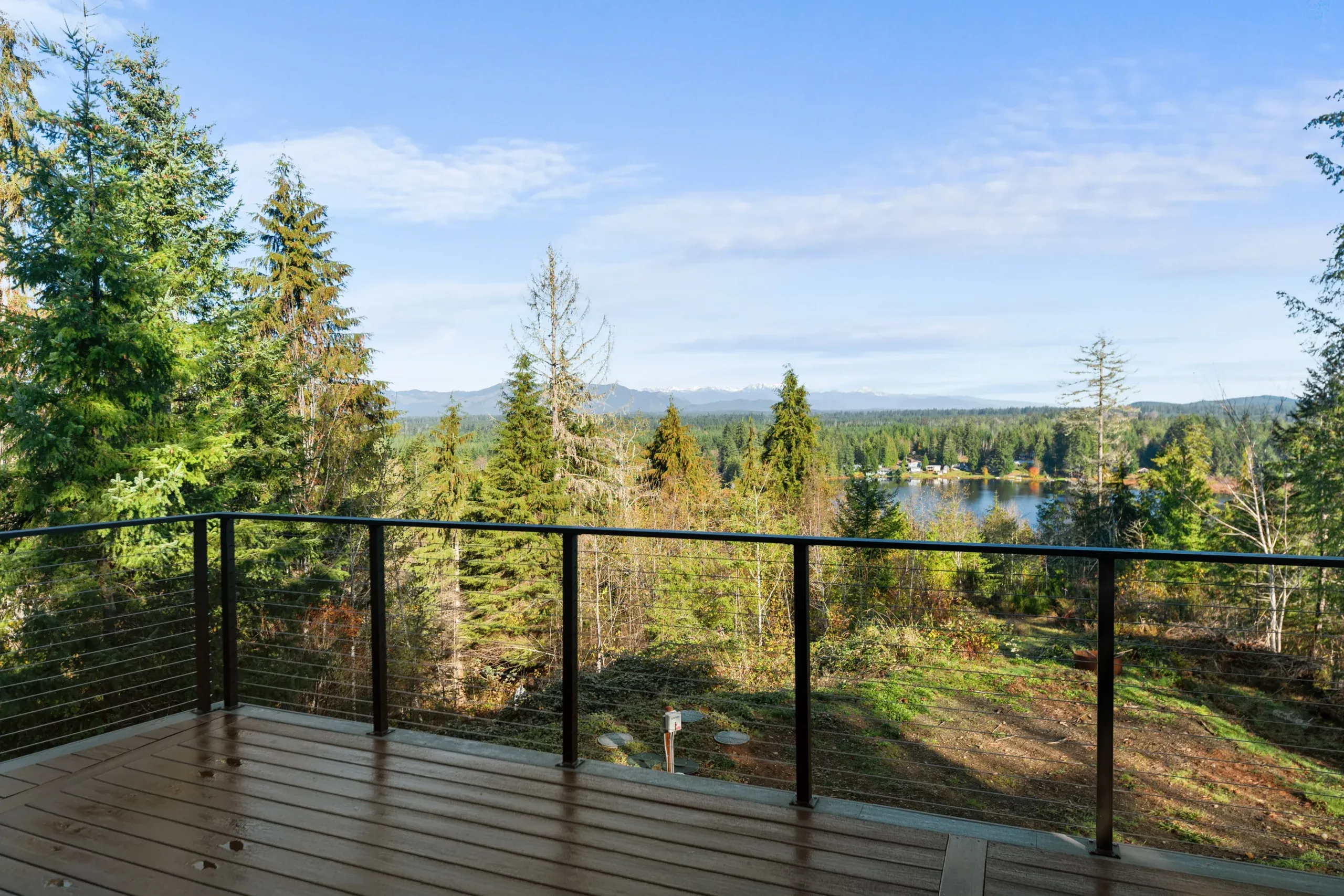 Wooden deck overlooking a forested landscape and distant hills under a bright blue sky
