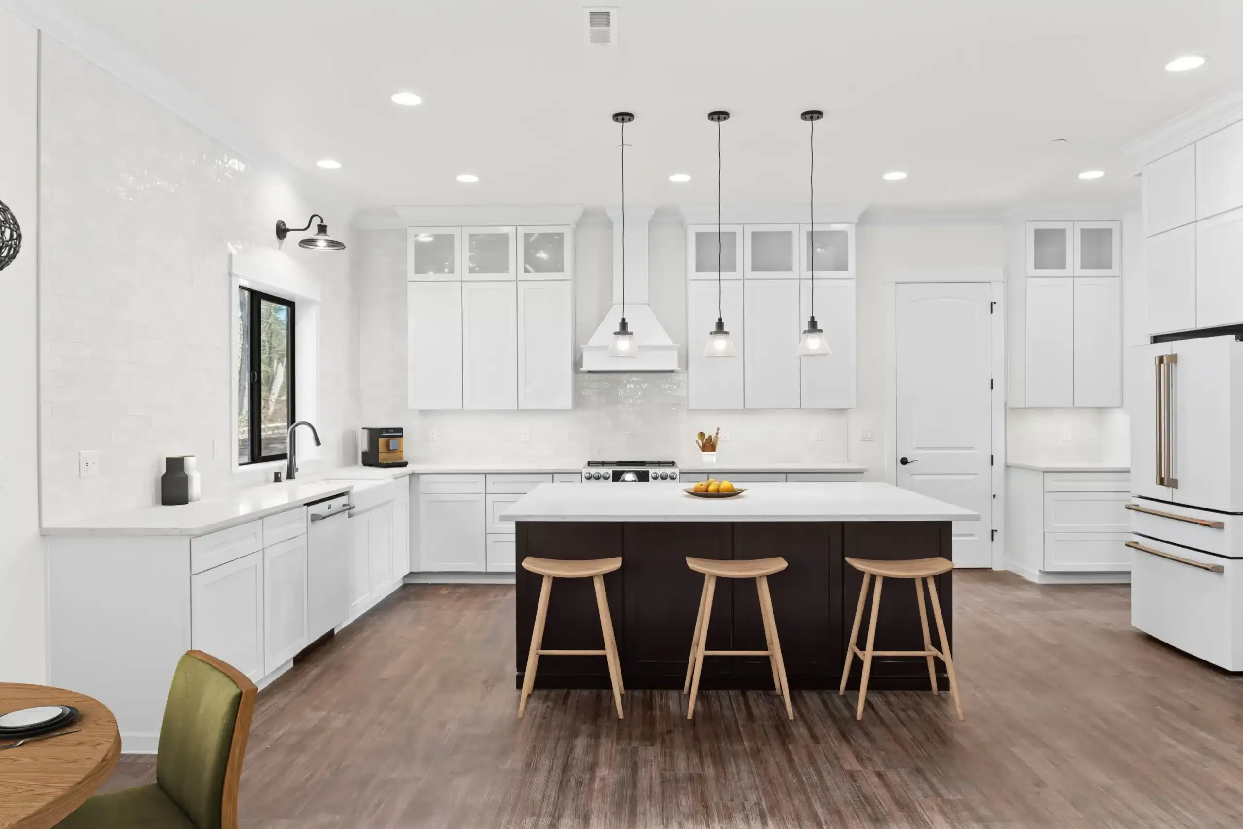 Bright white modern kitchen with black island, three stools, and wood floor